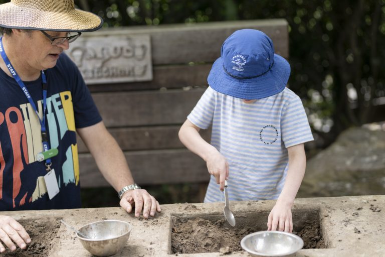 A male educator is supervising a child playing with mud and exploring texture
